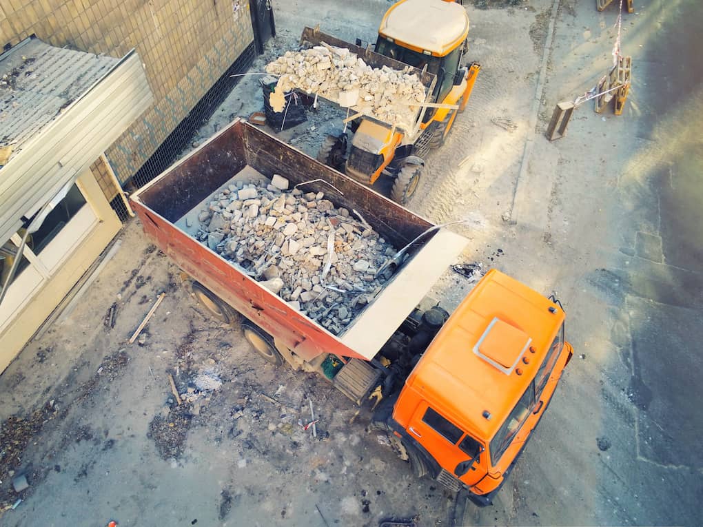loader uploading waste and debris into dump truck at construction site.