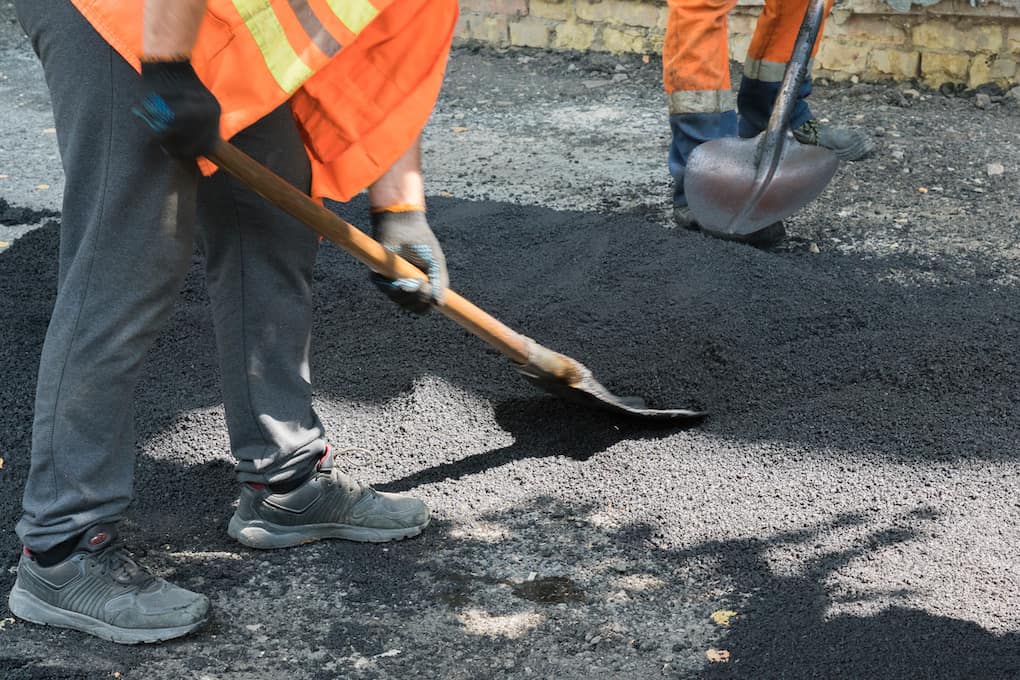 Worker man lays asphalt roading materials on parking lot