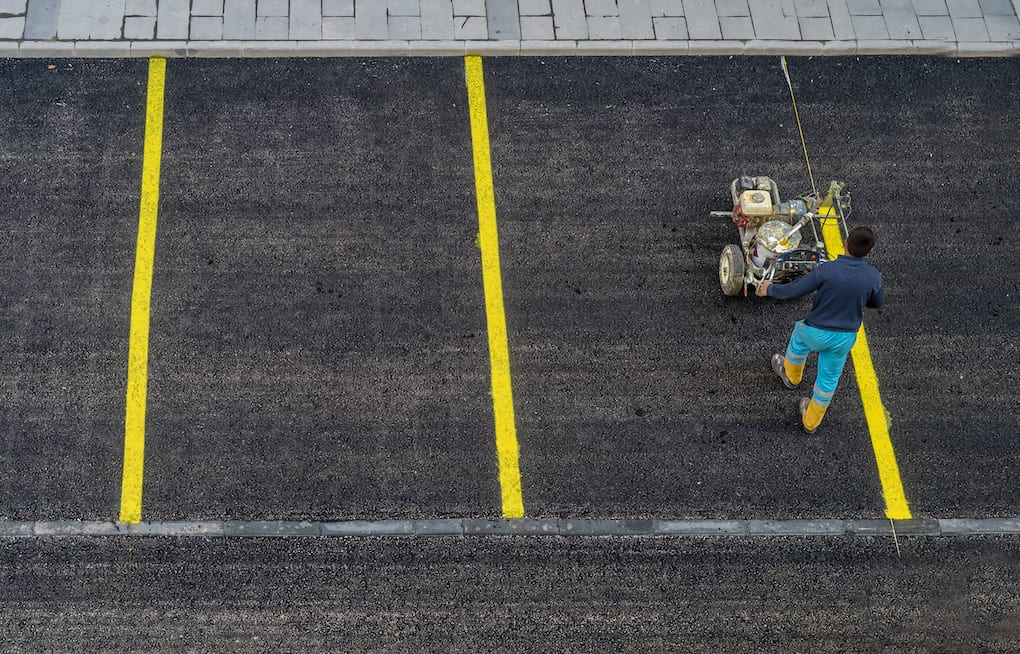 worker painting on yellow lines for asphalt roading materials parking lot
